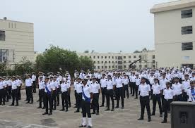 Students in white shirts and dark pants participating in school assembly outdoors.